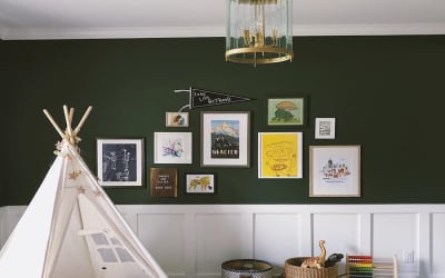 A Gallery Wall of photo prints, art and a pennant, hang in a green playroom with a toy tent.