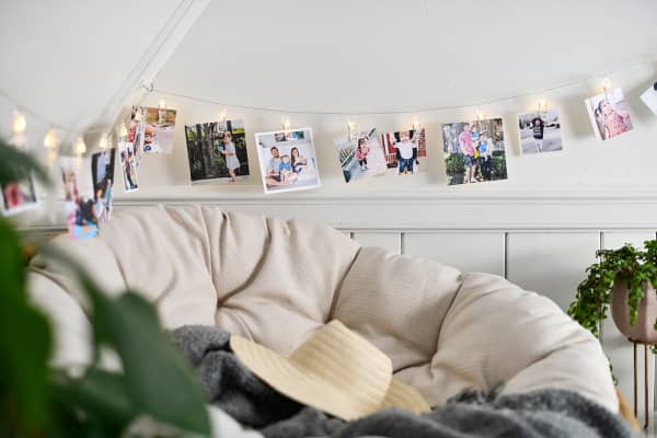 A string of LED lights that are also clips hold a collection of custom photo Square Prints on the wall of a cozy room.