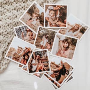 A set of Parabo Press Square Prints showing photos from a family photoshoot are scattered over an ivory knit blanket.
