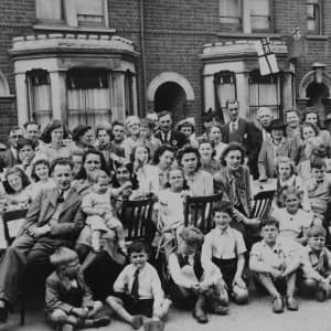 A black and white vintage image of a very large family gathered around a table outside in front of row houses.