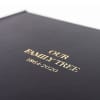 A close-up shows the texture on a black vegan leather covered Family History Book with a gold embossed title.