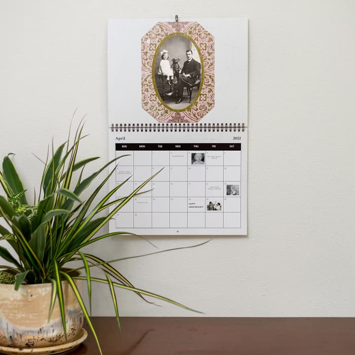 A Family History Wall Calendar showing a vintage family photo and important birthdays and anniversaries hangs near a houseplant.