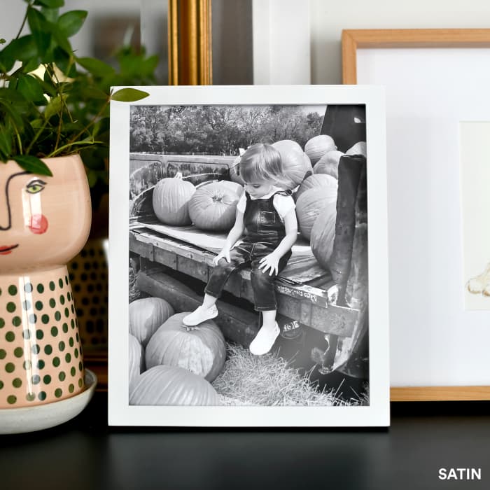 A black and white Fine Art Print showing a kid in a pumpkin patch, is on display in an 8x10 white frame.