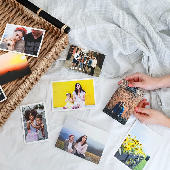 Eight 4x6 and 5x7 Classic Photo Prints scattered across a white bedsheet. Hands hold one of the photos.
