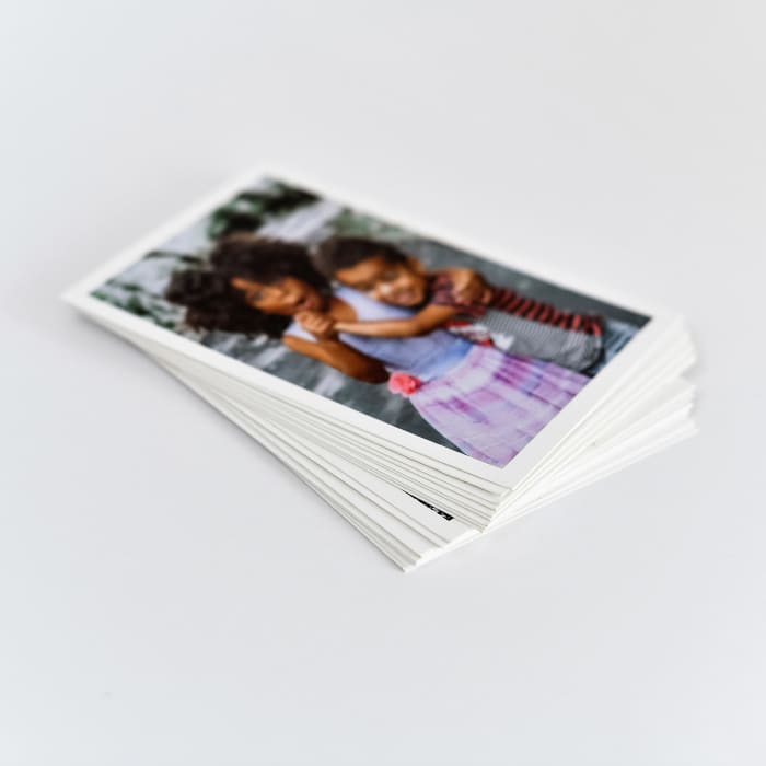A stack of Classic Prints with white borders. The top print shows two children hugging eachother.