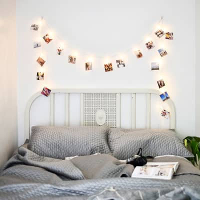 A 120 inch string of clothespin shaped clips that are also LED lights, hold up 20 Square Photo prints above a bed.
