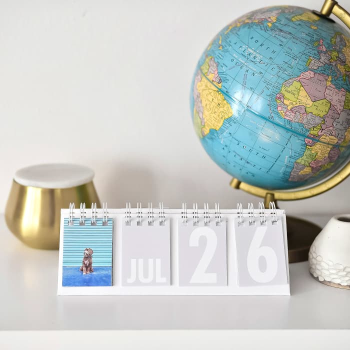 A Forever Desk Calendar displaying a puppy photo is placed on a desk beside a globe and several candles.