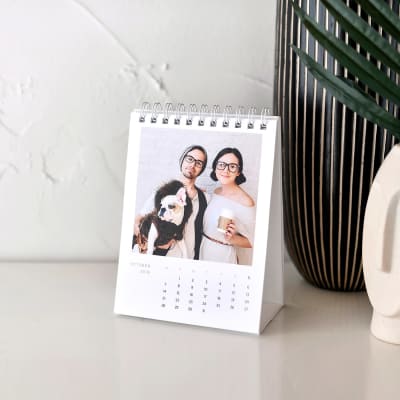 A Classic custom photo Desk Calendar is propped open beside a couple of decorative vases.