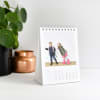 A Parabo Press custom photo Classic Desk Calendar is placed on a white desk, showing a cute family photo.