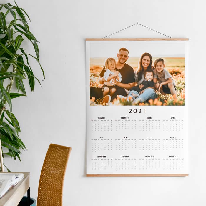 An Engineer Print Calendar hangs from oak Wood Poster Rails in an office. The calendar has one custom photo across the top of the print.