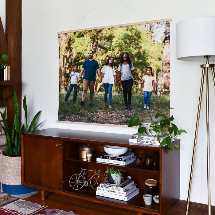 A 3x4 foot Engineer Print of a family holding hands hangs from Wood Poster Rails above a living room credenza.