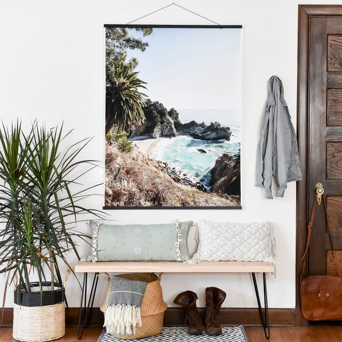An Engineer Print of a tropical vacation view hangs from Black Poster Rails above an entryway bench.