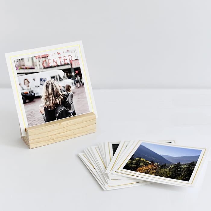 A stack of 4x4 inch gold Foil Bordered Square Prints sit beside a photo displayed in a Wood Block.