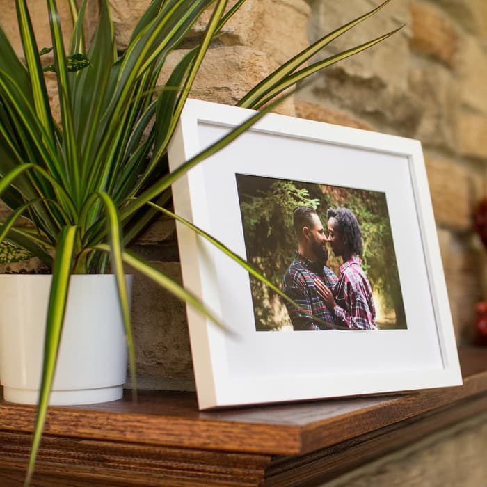 A photo of a couple is displayed as a Framed Fine Art Print in a black frame with a white mat, on a mantle.