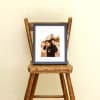 A Framed Fine Art Print in Black sits on a wooden chair and shows a father son photo.