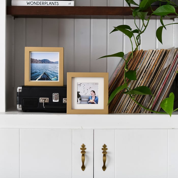 Two Gold Square frames accompany a record collection on top of a cabinet. 