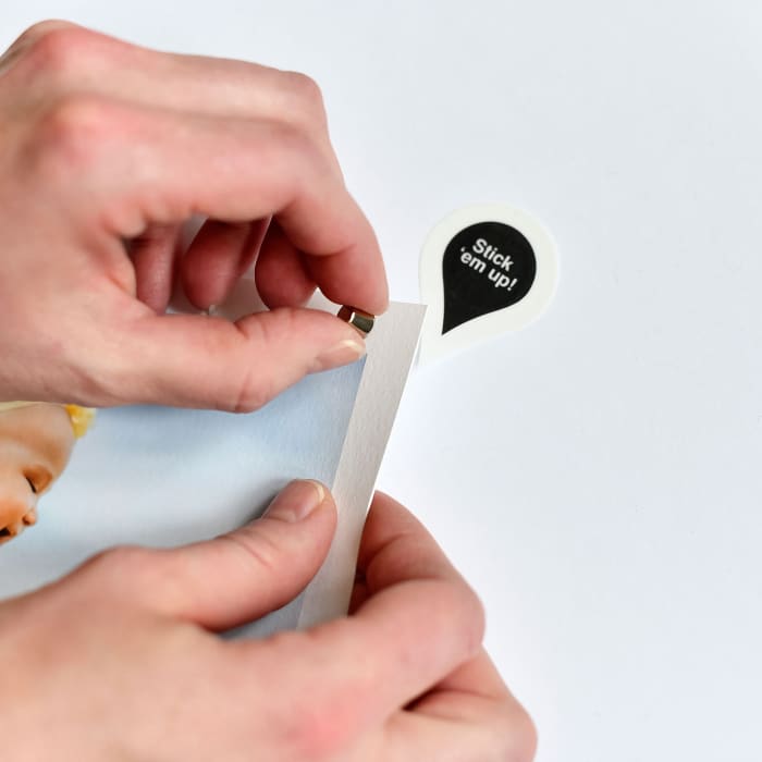Hands place a Newsprint and Good Hangup magnet onto a magnetic sticker.