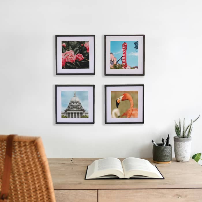Four black framed photo prints hang in a square grid on the wall above a desk.