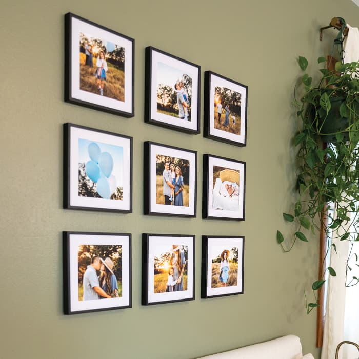 Nine black framed photo prints of a maternity photo shoot hang in a grid shape above a bed, with a hanging plant nearby.