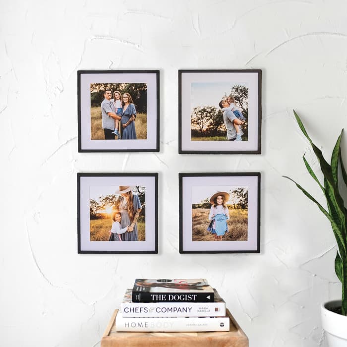 Four black framed photo prints of a maternity photo shoot hang in a grid above a stack of books.
