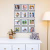 Twelve monthly photos of a baby are displayed in black frames hung in a photo grid above a dresser in a nursery.