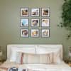 Nine black framed photo prints of a maternity photo shoot hang in a grid shape on a green wall above a bed.