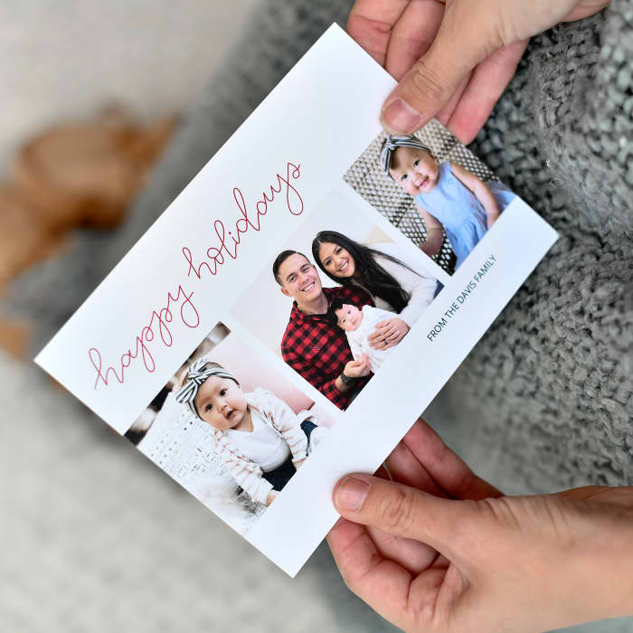 Hands hold a 5x7 Holiday Card showing three family photos on top of a cozy knitted blanket.