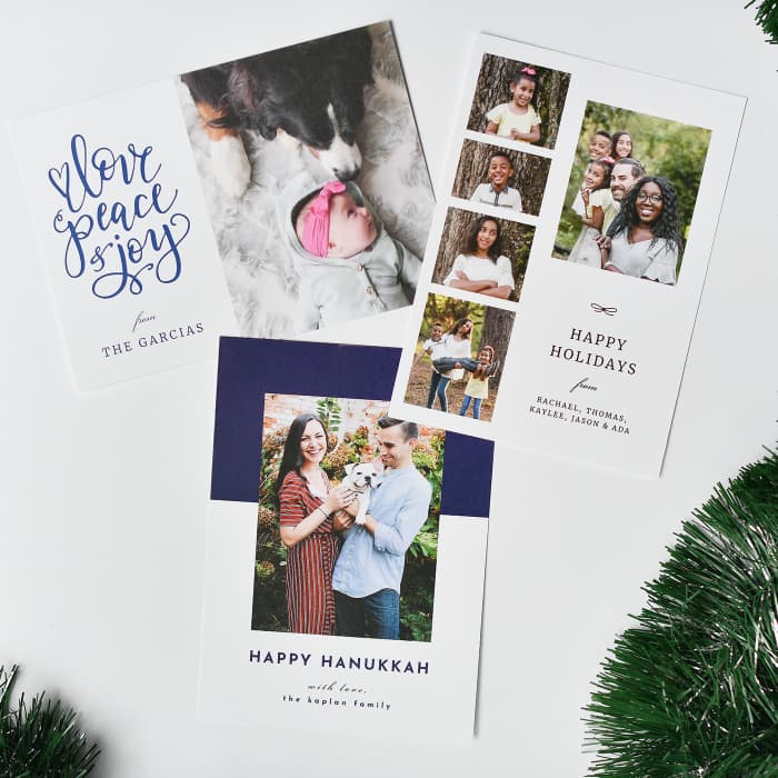 Three styles of 5x7 Holiday Cards with custom photos and messages, are spread among tinsel and garland.