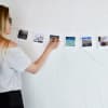 A woman hangs vacation photos from a Horizontal Photo Rope, a white wire strung across the wall.