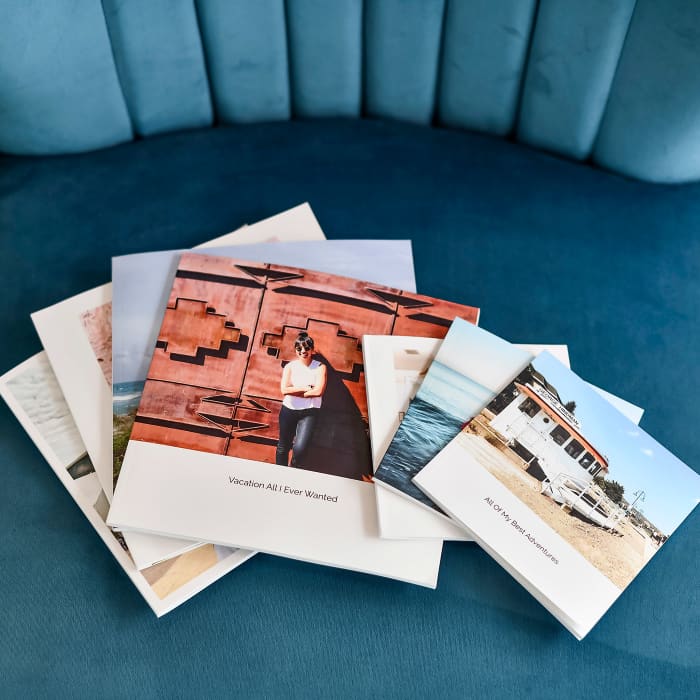 Softcover Photo Books of varying sized are fanned out across the seat of a teal velvet chair.