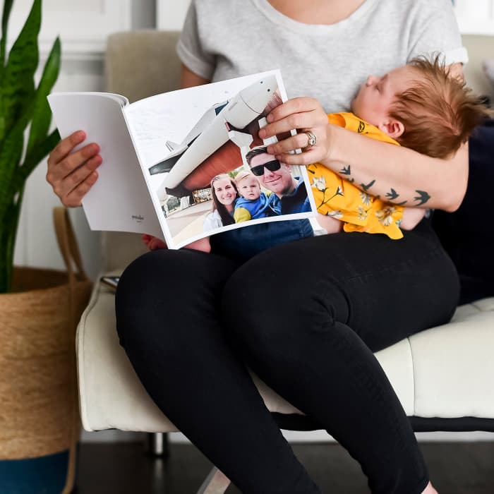 A woman holds a baby in her lap as she flips through a Softcover Photo Book with a family on the cover.