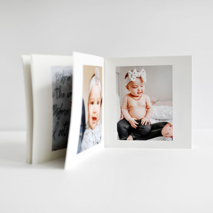 A small Softcover Photo Book showing baby photos, is displayed on a white table.
