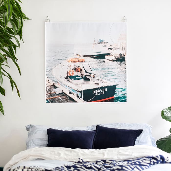 A Square Engineer Print of a photo of a boat, hangs above a bed from a set of Skeleton Clips.