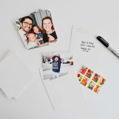 A stack of 5.75 inch Square Envelopes and photo prints are being prepared to be mailed.