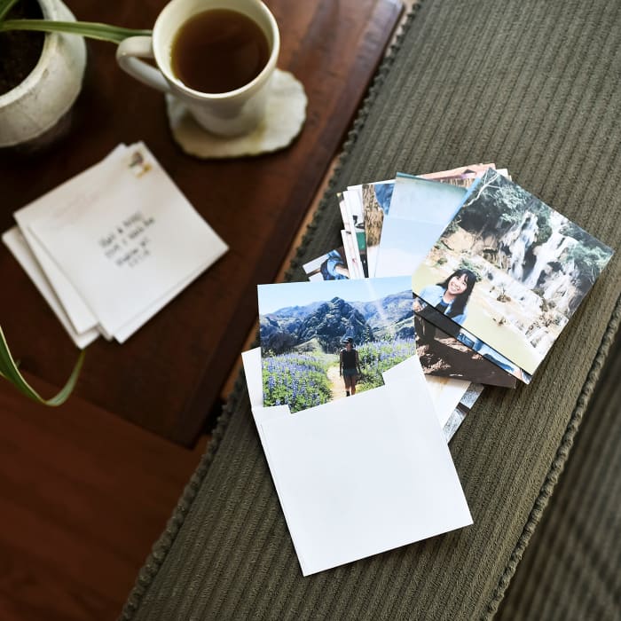 A stack of photo prints and a set of 4.25 inch Square Envelopes are placed on the coffee table.