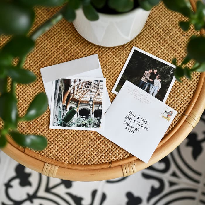A pair of white bordered photo prints and Square Envelopes sit on a rattan side table.