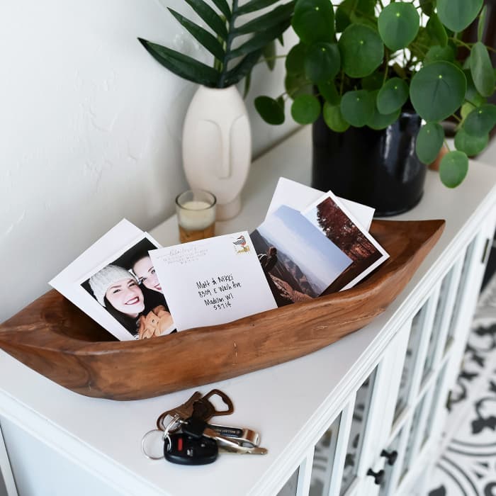A wooden bowl holds an assortment of photos and Square Envelopes on an entryway cabinet.