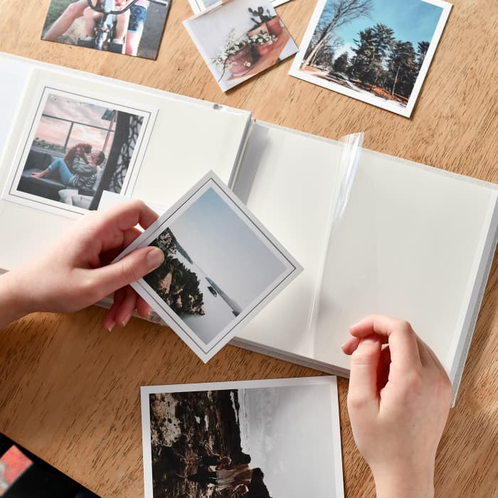 Two hands lift a plastic page cover to place vacation photos into a Parabo Press Square Print Photo Album.