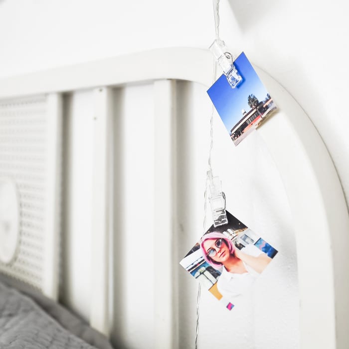 A close up of two Tiny Photo Prints hanging from Clip Lights on a bedframe.