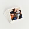 A stack of white bordered Tiny Prints on a white background. The top print shows a toddler learning how to play guitar.