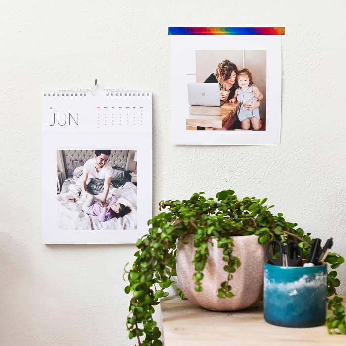A Keepsake Wall Calendar hangs above a desk. The square photo portion of a calendar page is hanging on the wall.