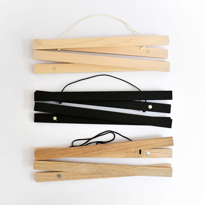Light wood Maple, painted Black, and darker wood Oak Poster Rails show the magnets inside that help them hang prints damage-free.