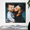 A 24x24 inch Gallery Wrapped Canvas Print of a kid and a donut hangs beside a bookshelf in a living room.